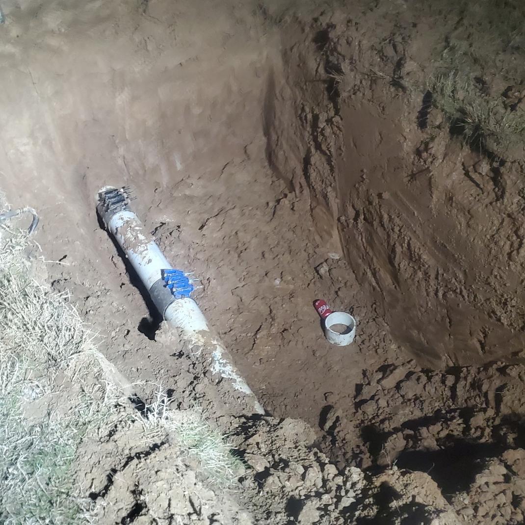 A partially buried pipe inside a hole dug into dirt