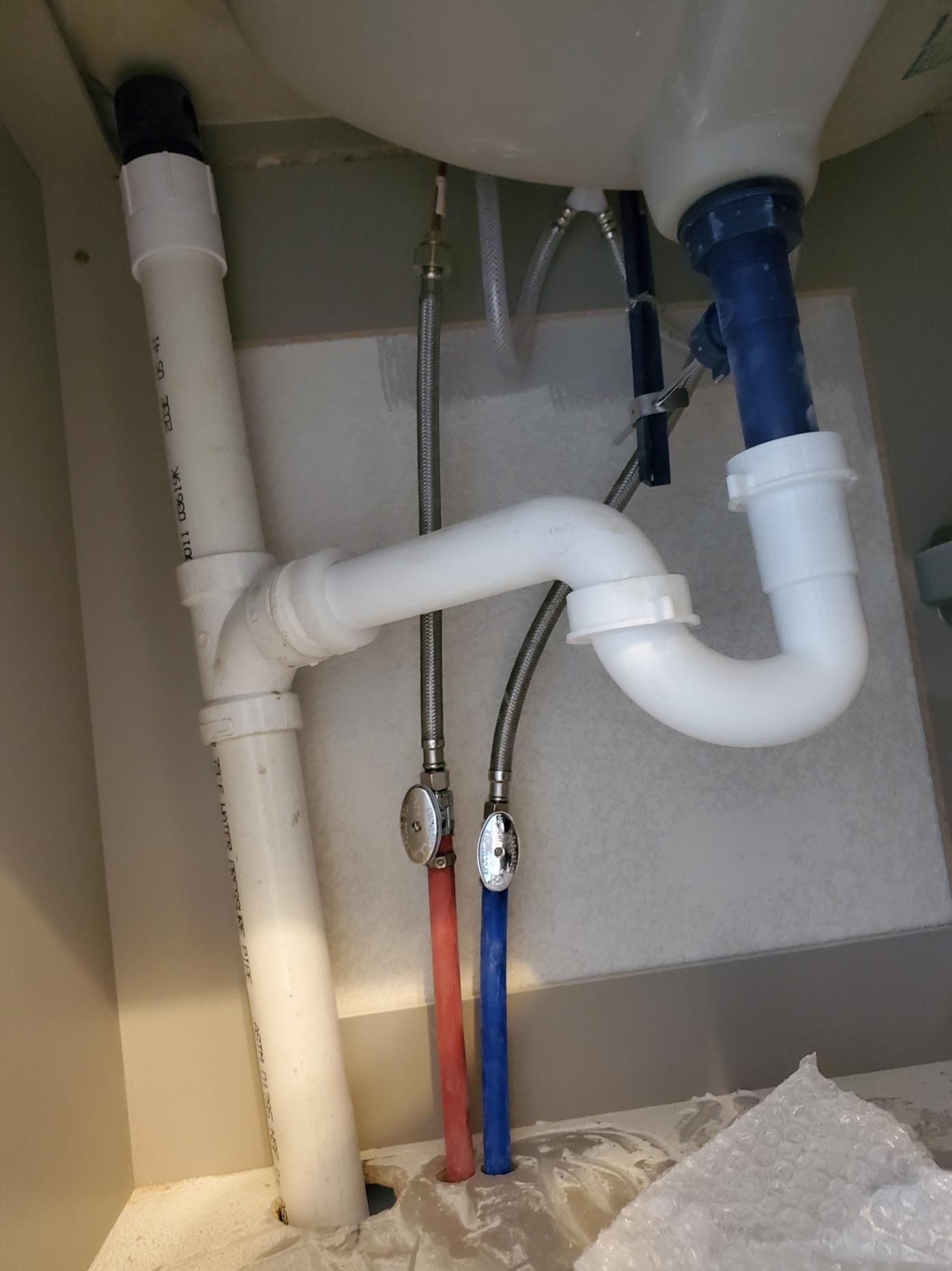 The underside of a sink, showing white and blue piping attached to the basin